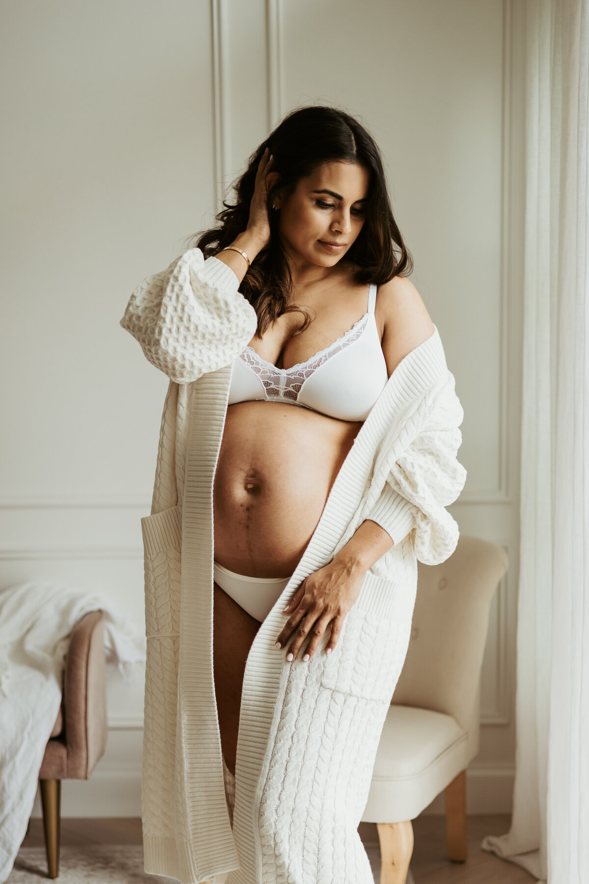 Pregnant mother in her Sydney loungeroom in white underwear and cardigan posing for her maternity photoshoot
