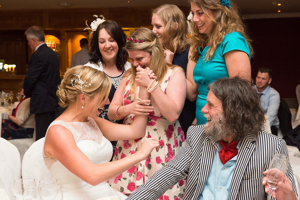 blonde bride sharing a fun time with her friends at her wedding reception in the Dingle Skellig Hotel while sitting beside a man with a black and white striped jacket and red cravat