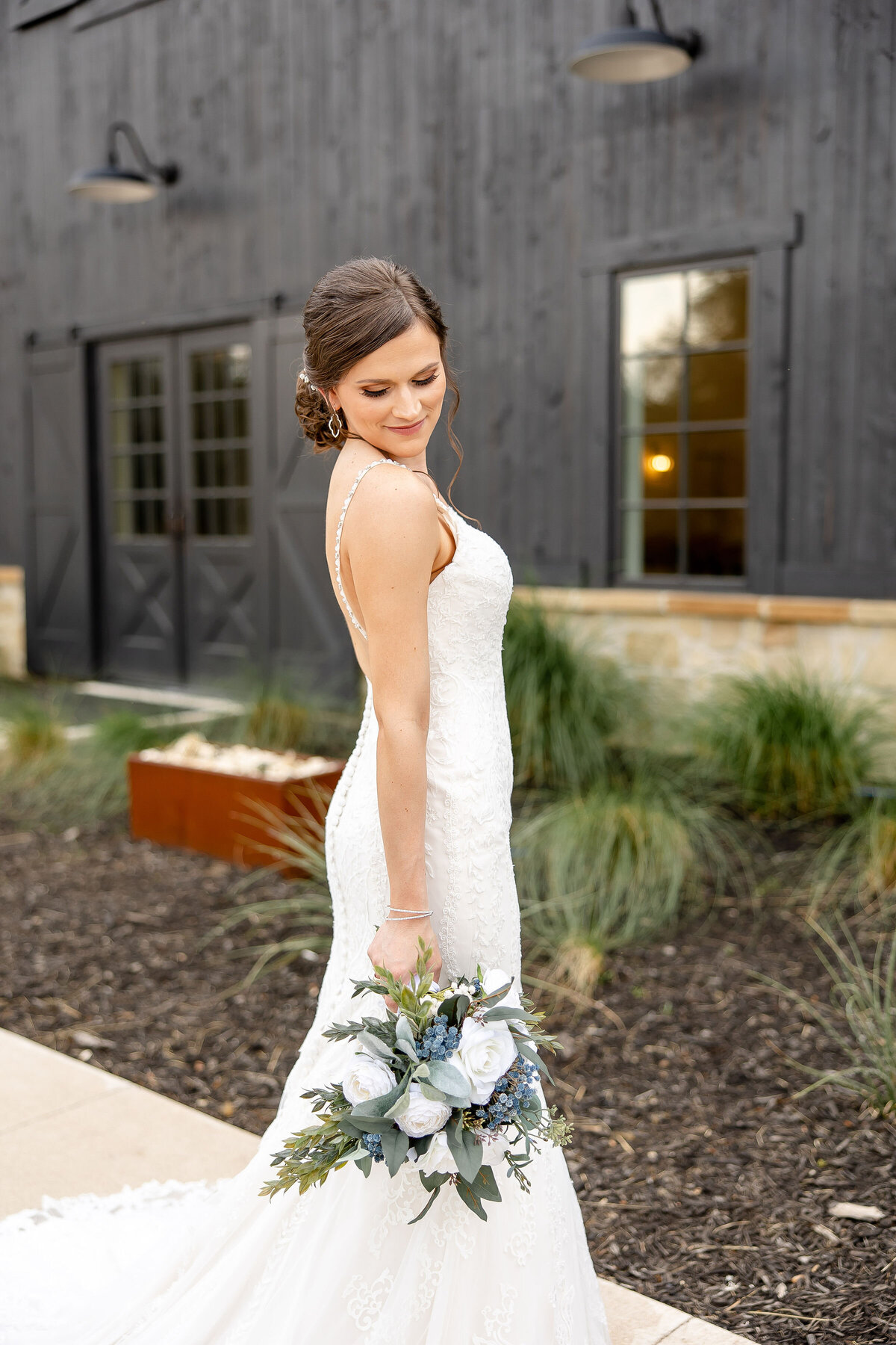 bride looks over shoulder holding bouquet in right hand at Morgan Creek Barn in Dripping Springs Texas