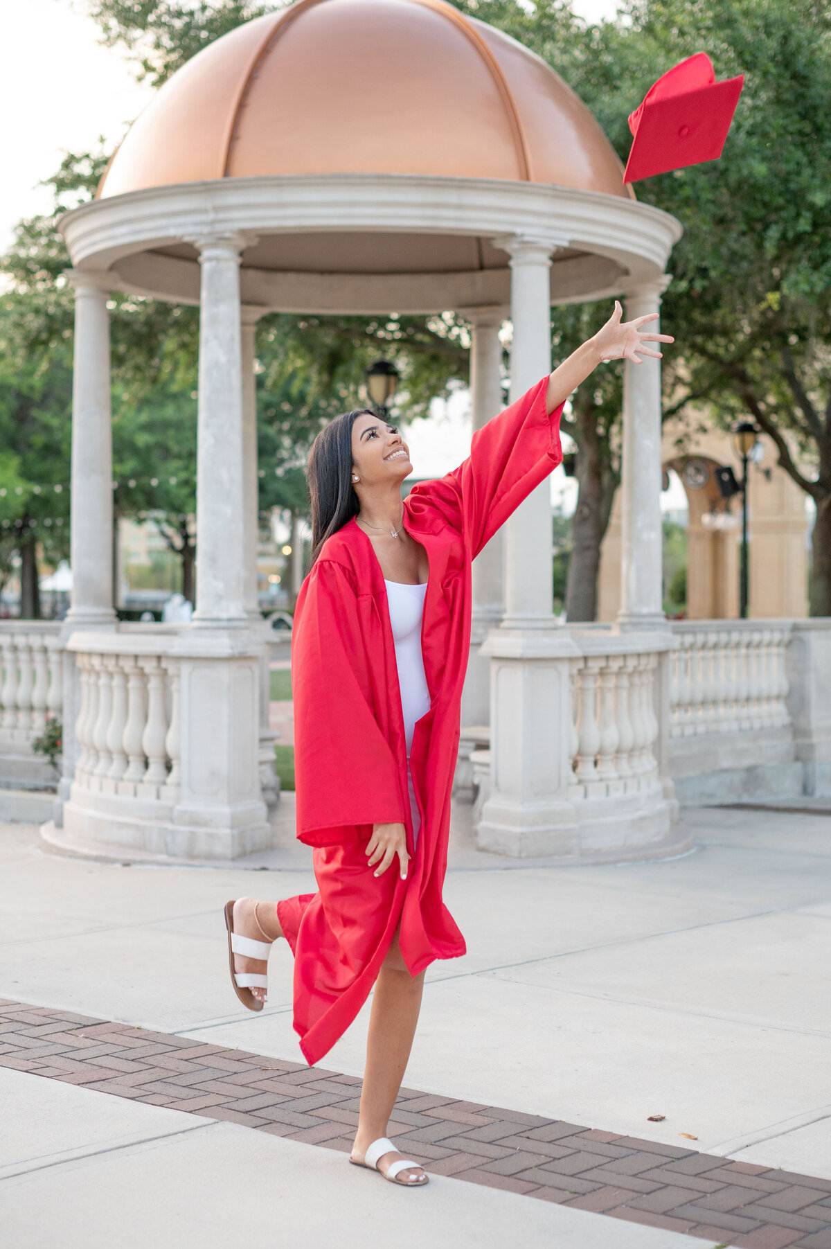 High school senior girl in graduation gown throws cap into the air.