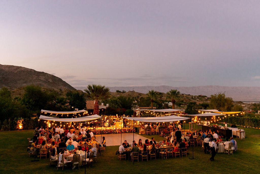 Outdoor wedding reception set up on the California cost. Every table has a white cloth canopy above with pretty twinkling yellow hanging lights.
