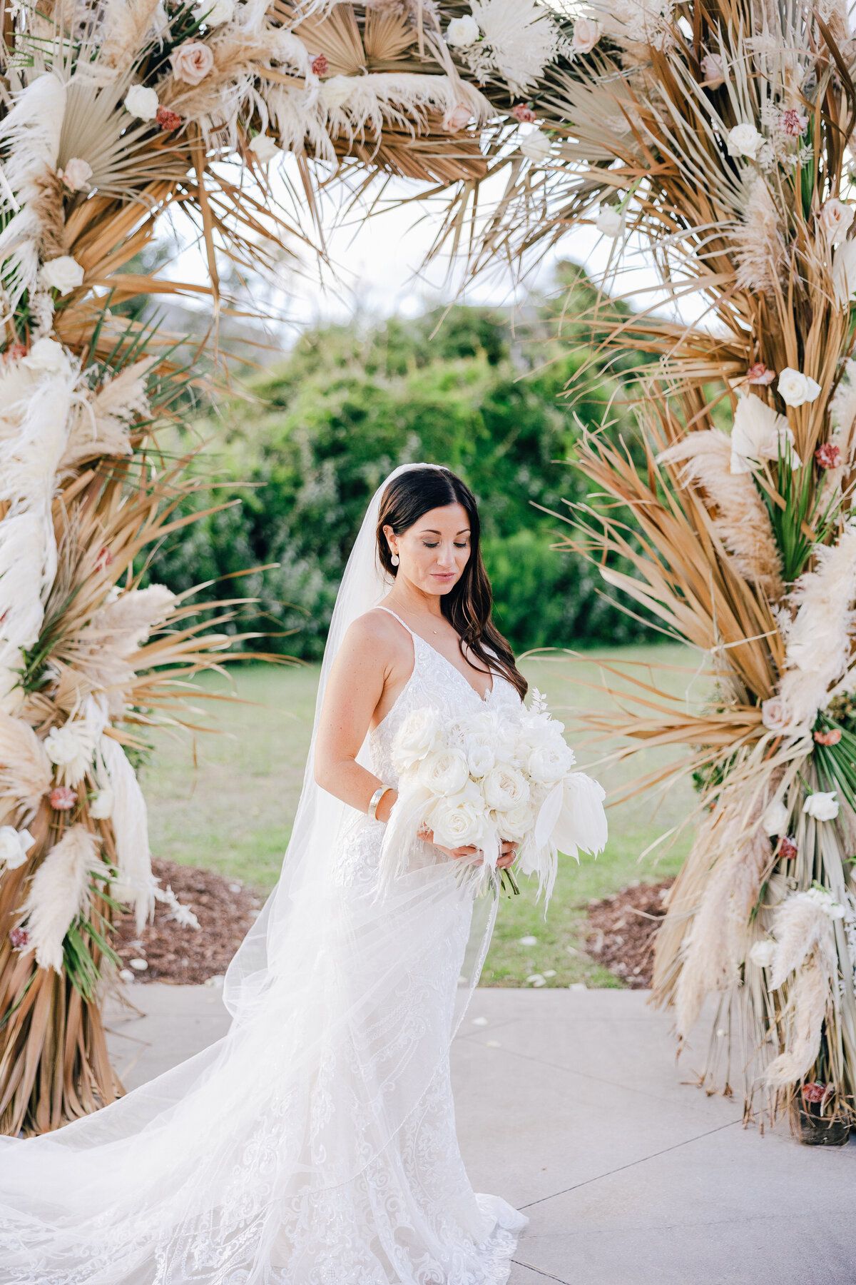 Bride in white dress holding a bouquet under a floral archway, captured by a Destination Wedding Photographer.