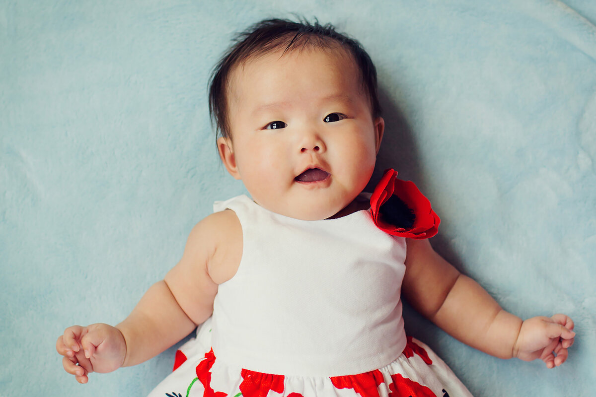 Sweet, chubby baby with dark hair and eyes and a red and white dress on a blue blanket from a photo session in Indy.