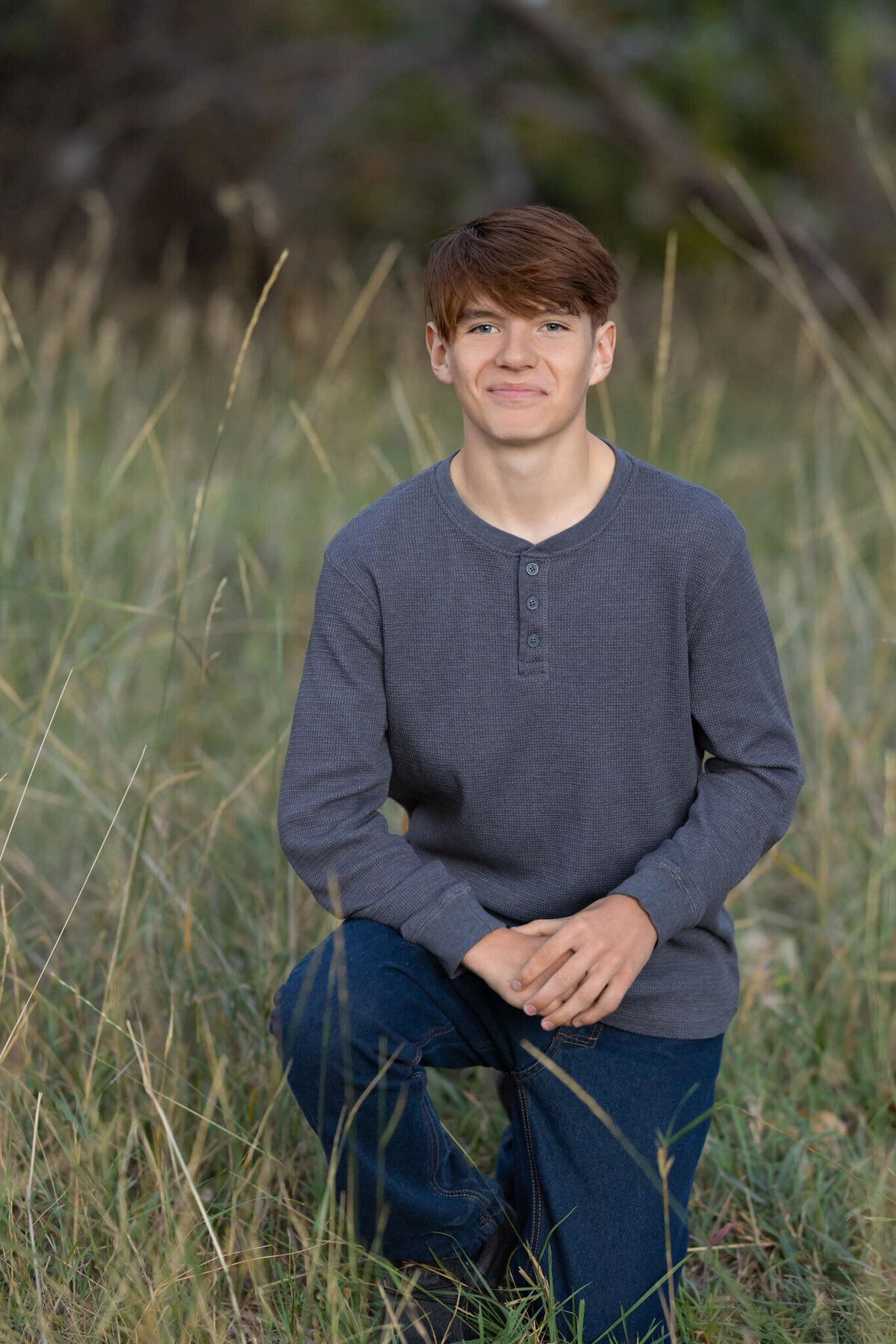 a young man kneeling in tall grass