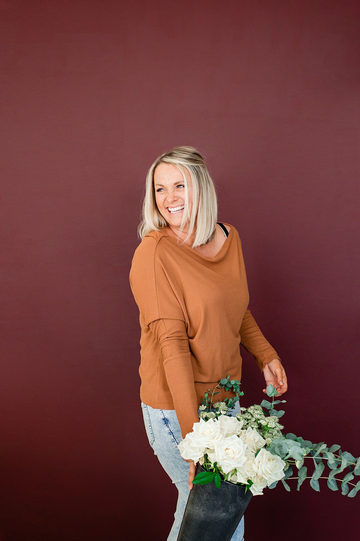 Florist standing in front of a maroon wall holding a bucket of flowers and laughing