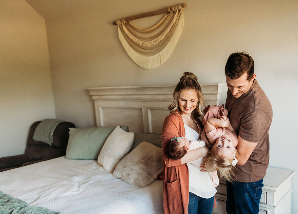 Newborn Photographer, Family of four standing up and playing with their toddler while snuggling their baby on the bed.