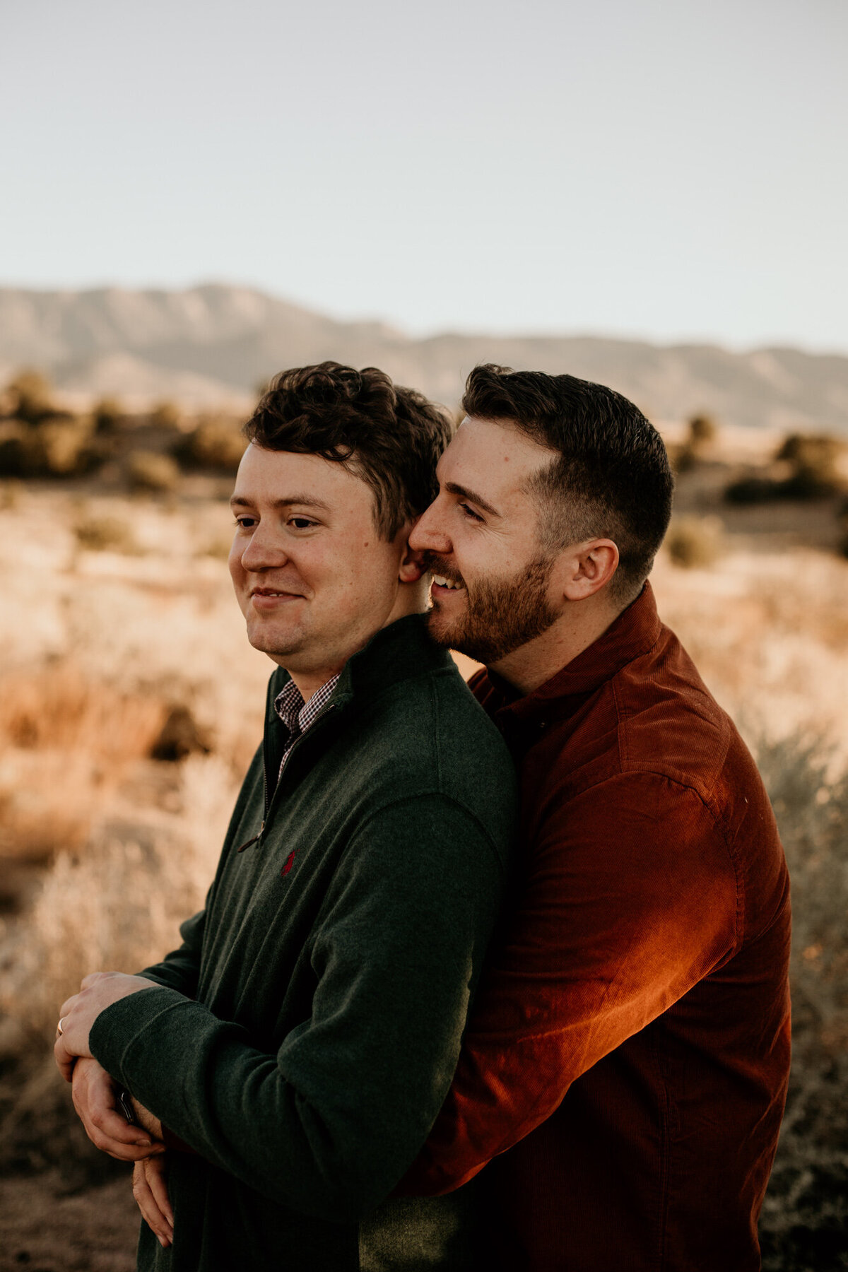 man whispering to same sex fiancé's ear from behind