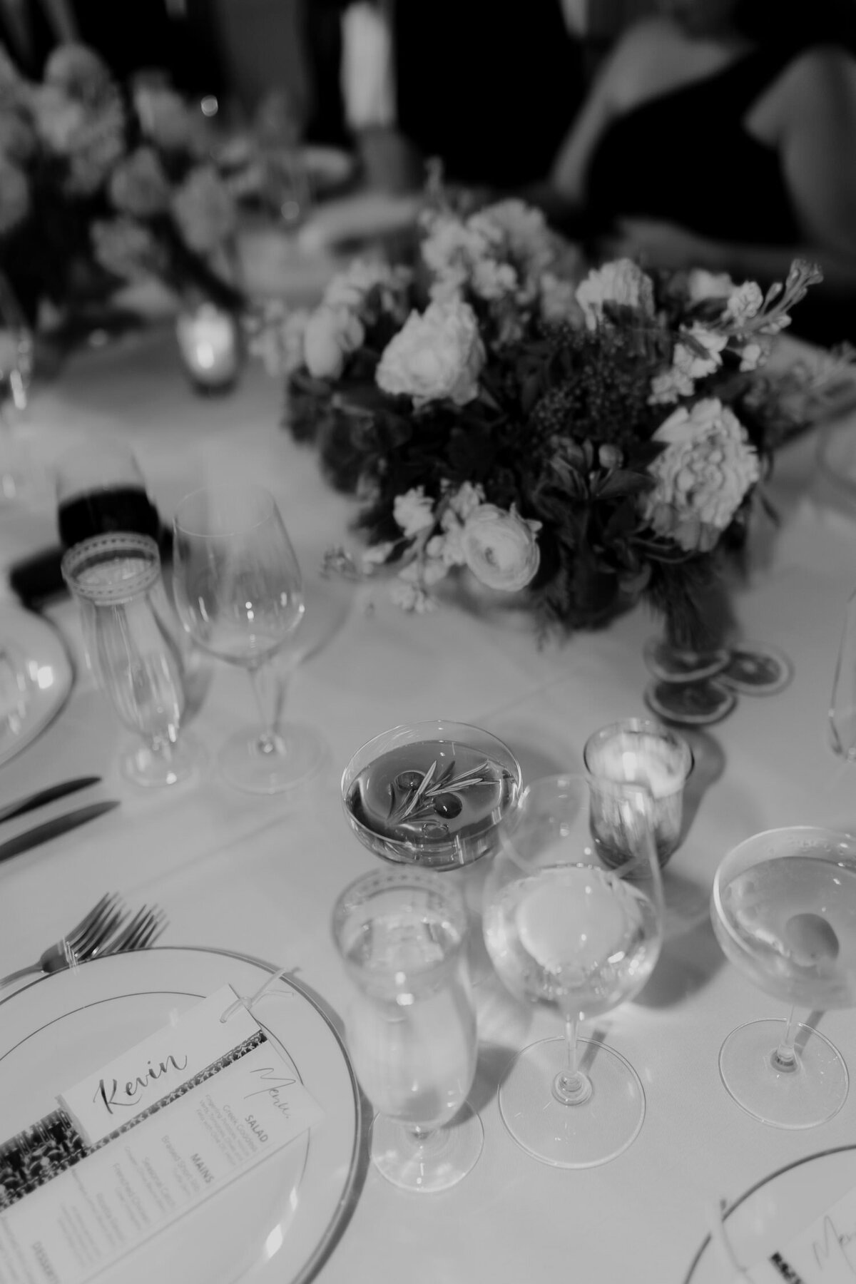 Black and white photo of wedding reception table with minimalistic flower arrangement, glasses and menu