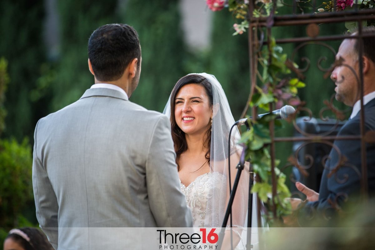 Bride smiles at her Groom at the altar as he takes a vow to her