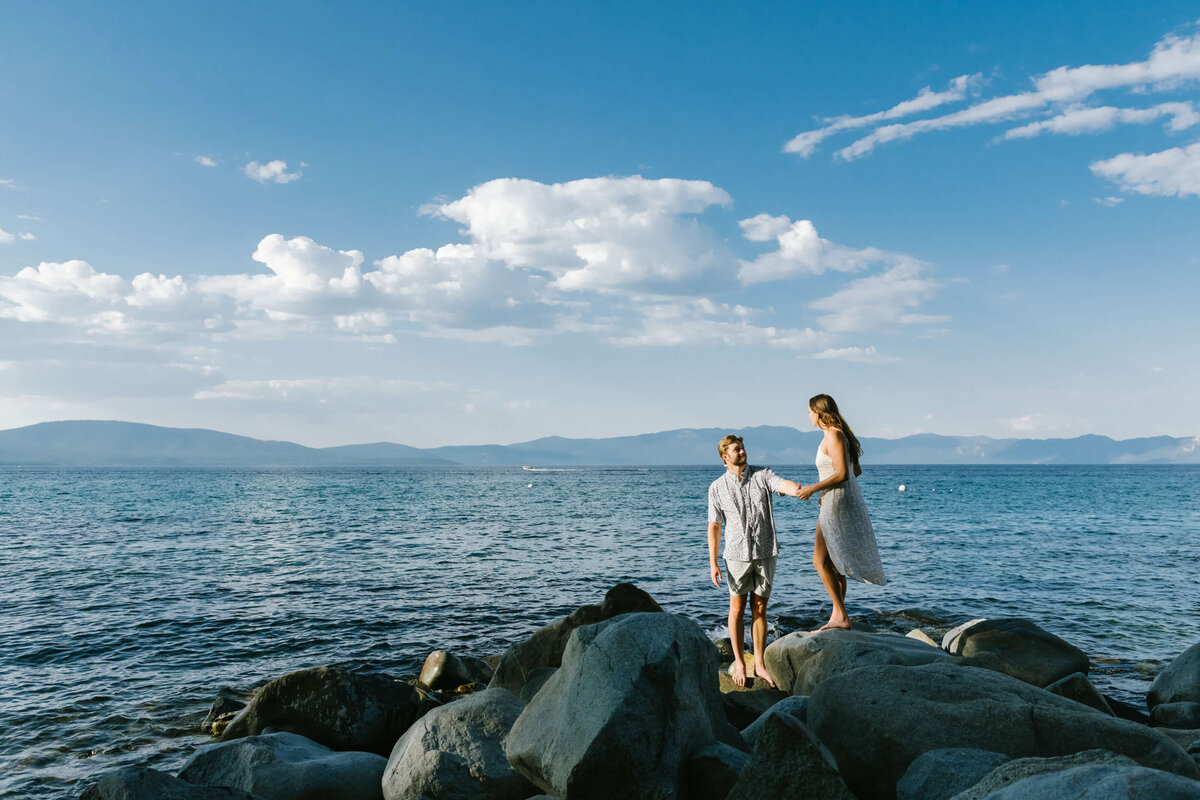 couple on rocks in Lake Tahoe with blue skies and puffy white clouds