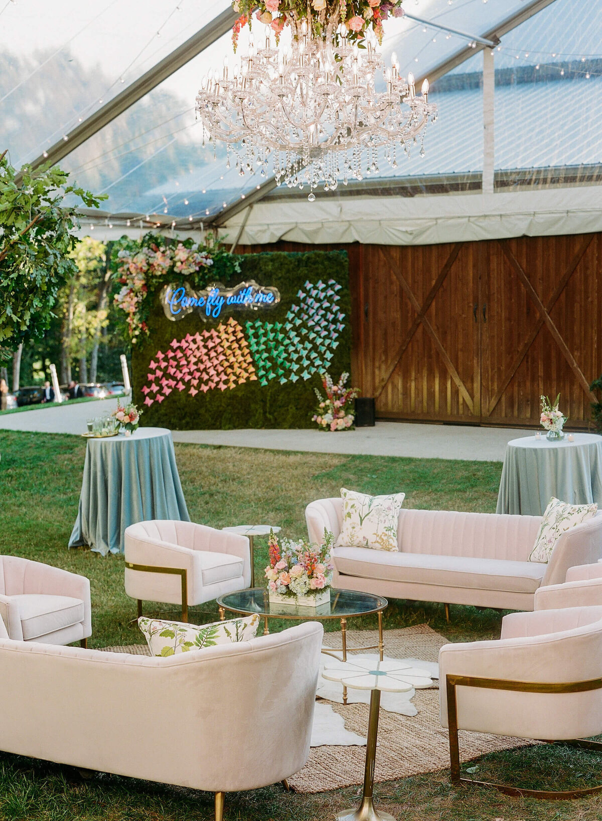Wedding cocktail hour under a tent with pink sofas and velvet blue linens.