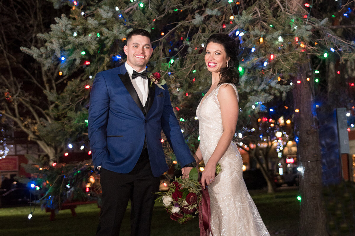 Bride and groom smile in front of holiday lights at their wedding