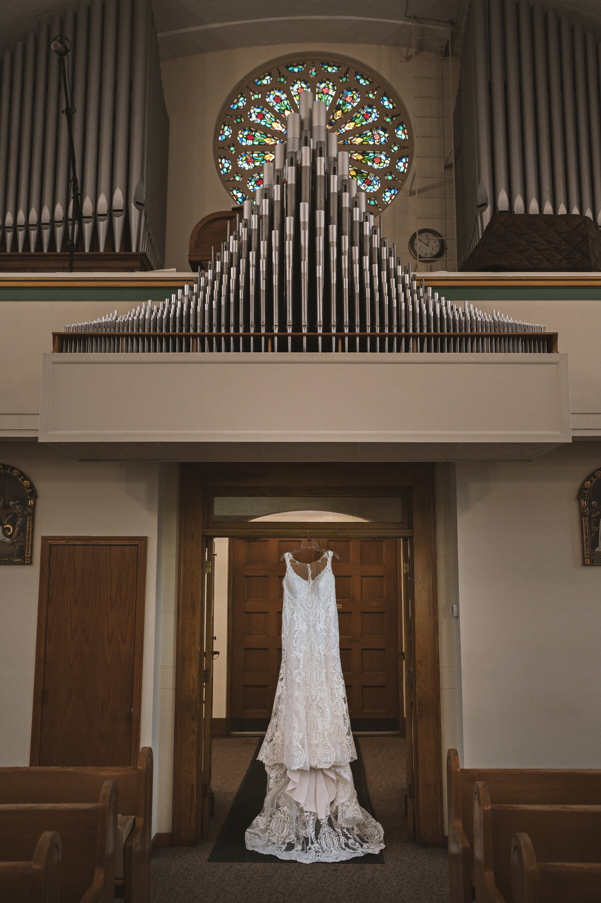 Wedding dress hanging in church below stained glass window.