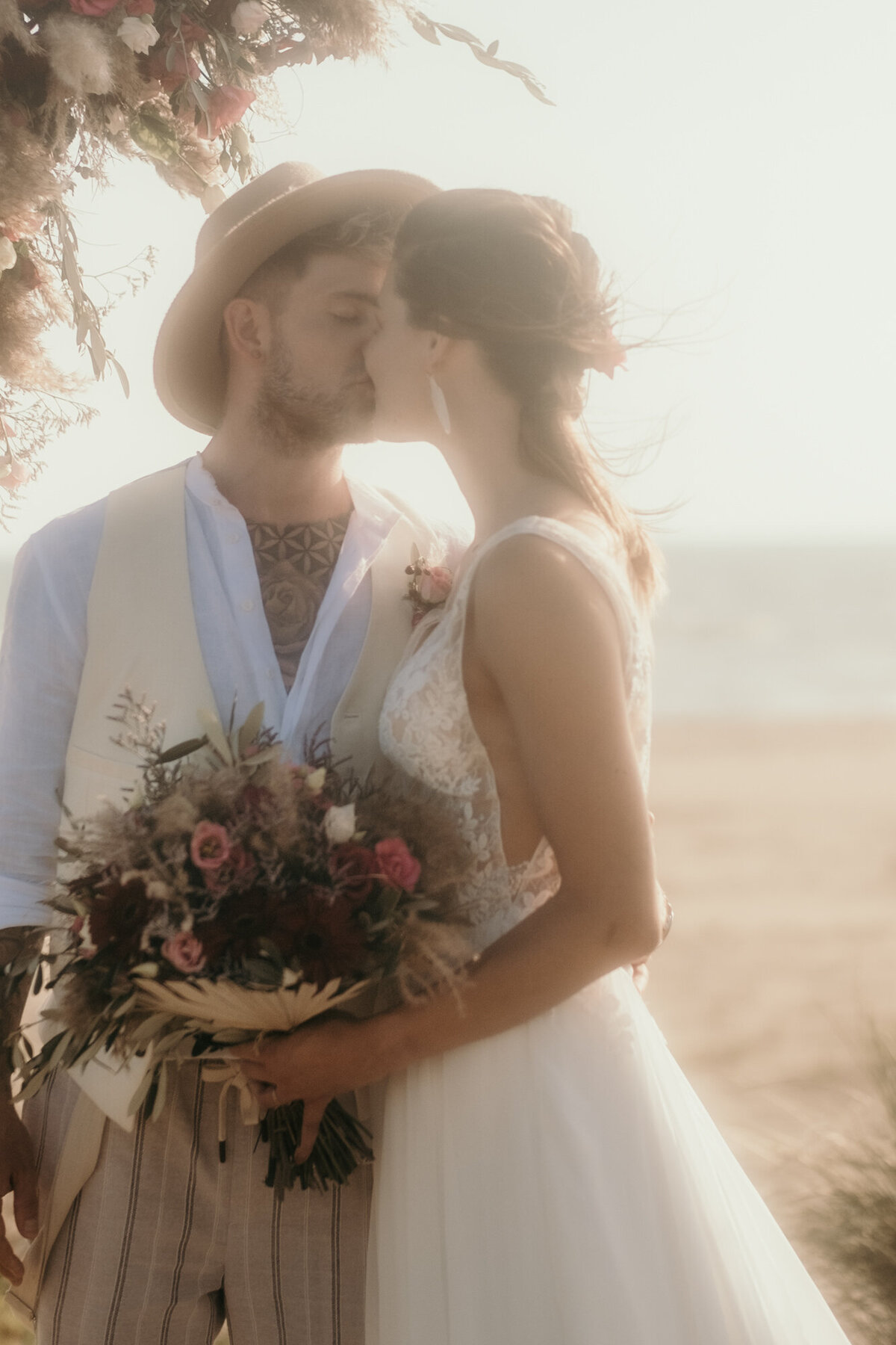 Das Hochzeitspaar küsst sich liebevoll. Im Hintergrund sieht man den Strand und das Meer.