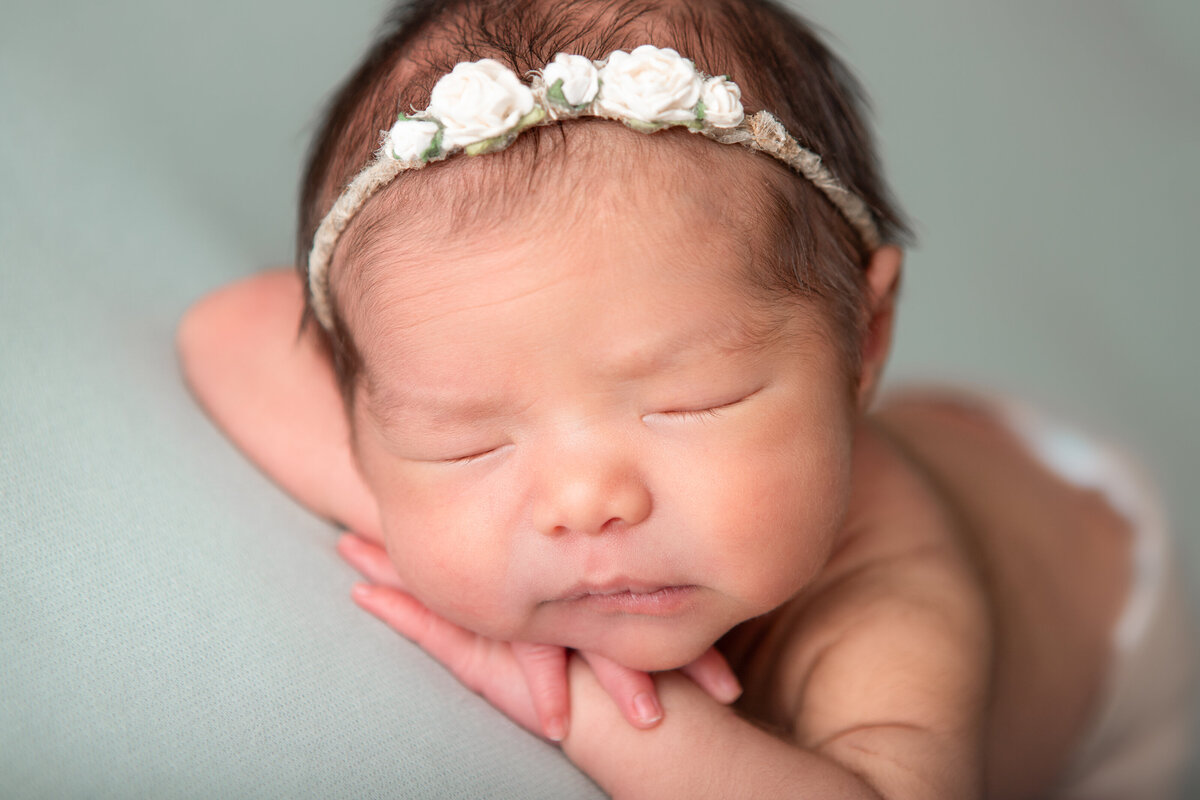 Chin on hands studio newborn pose on a mint backdrop