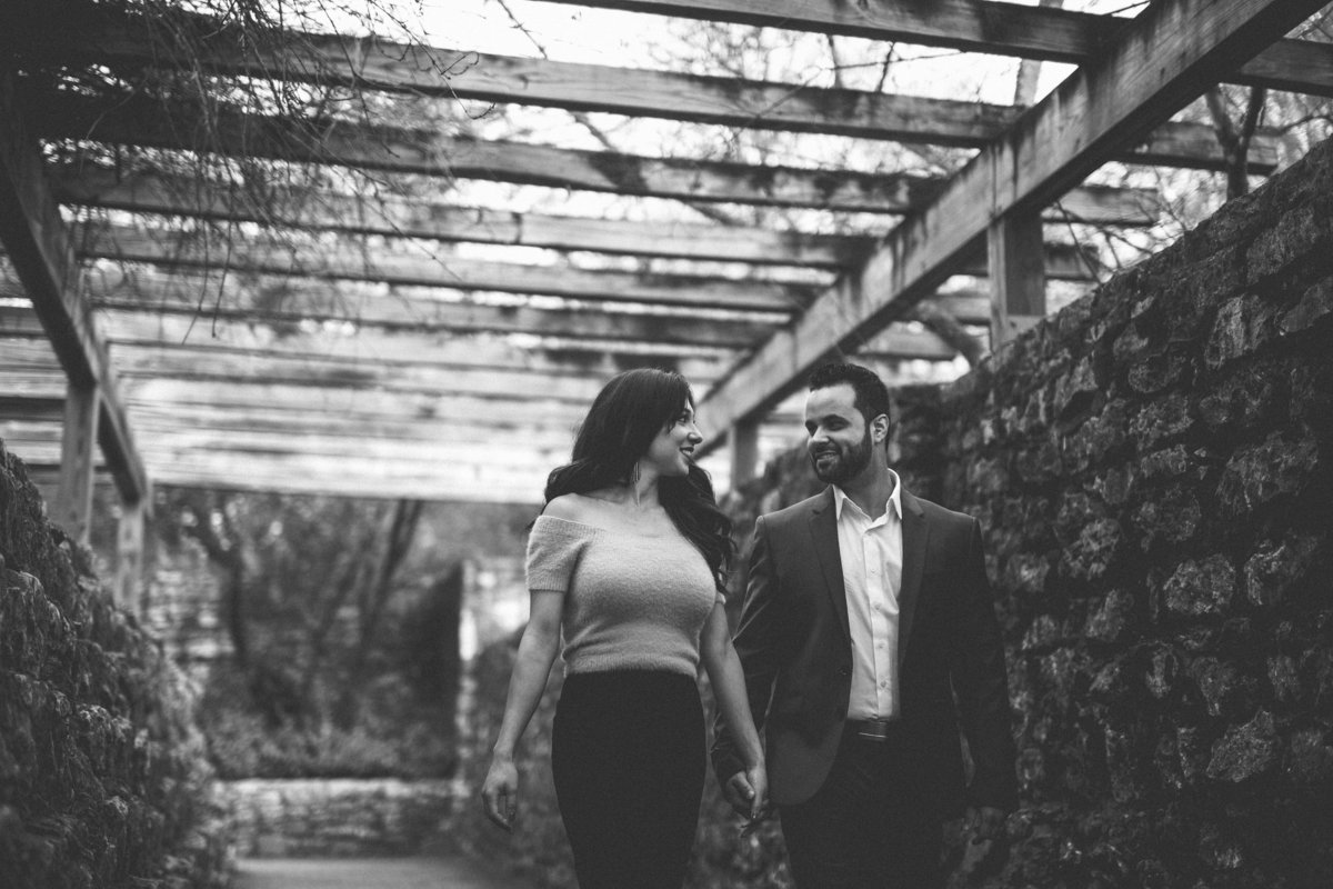 Black and white photo of couple walking under covered garden on their engagement session at the San Antonio Botanical Garden.