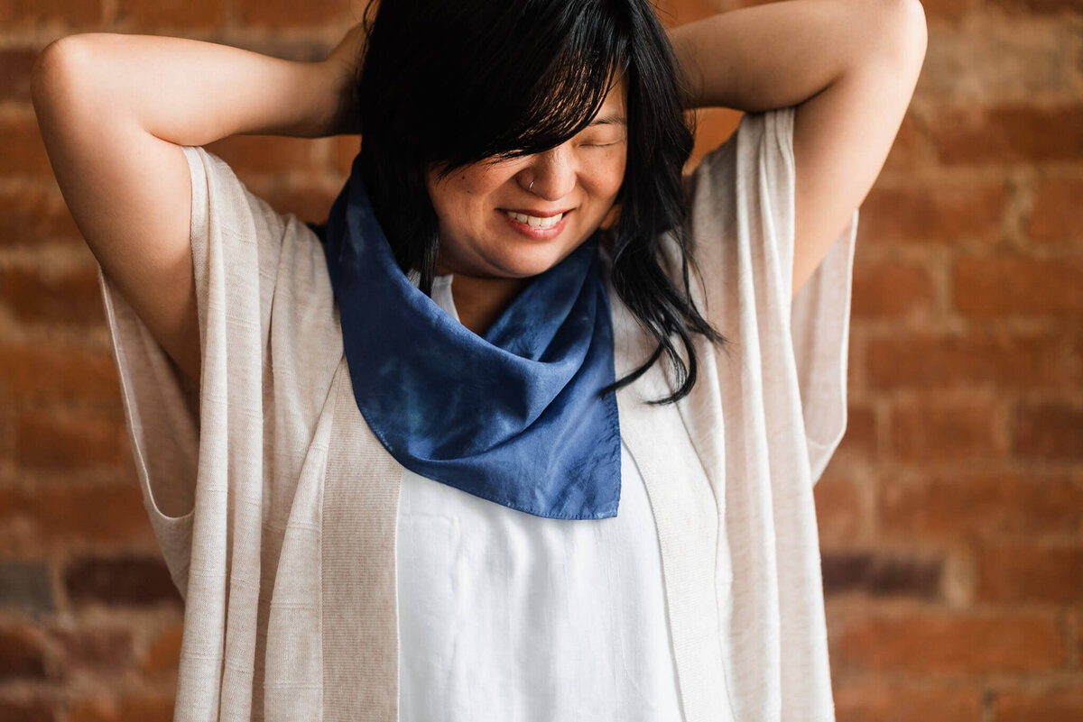 A smiling woman wrapping a silk bandana around her neck