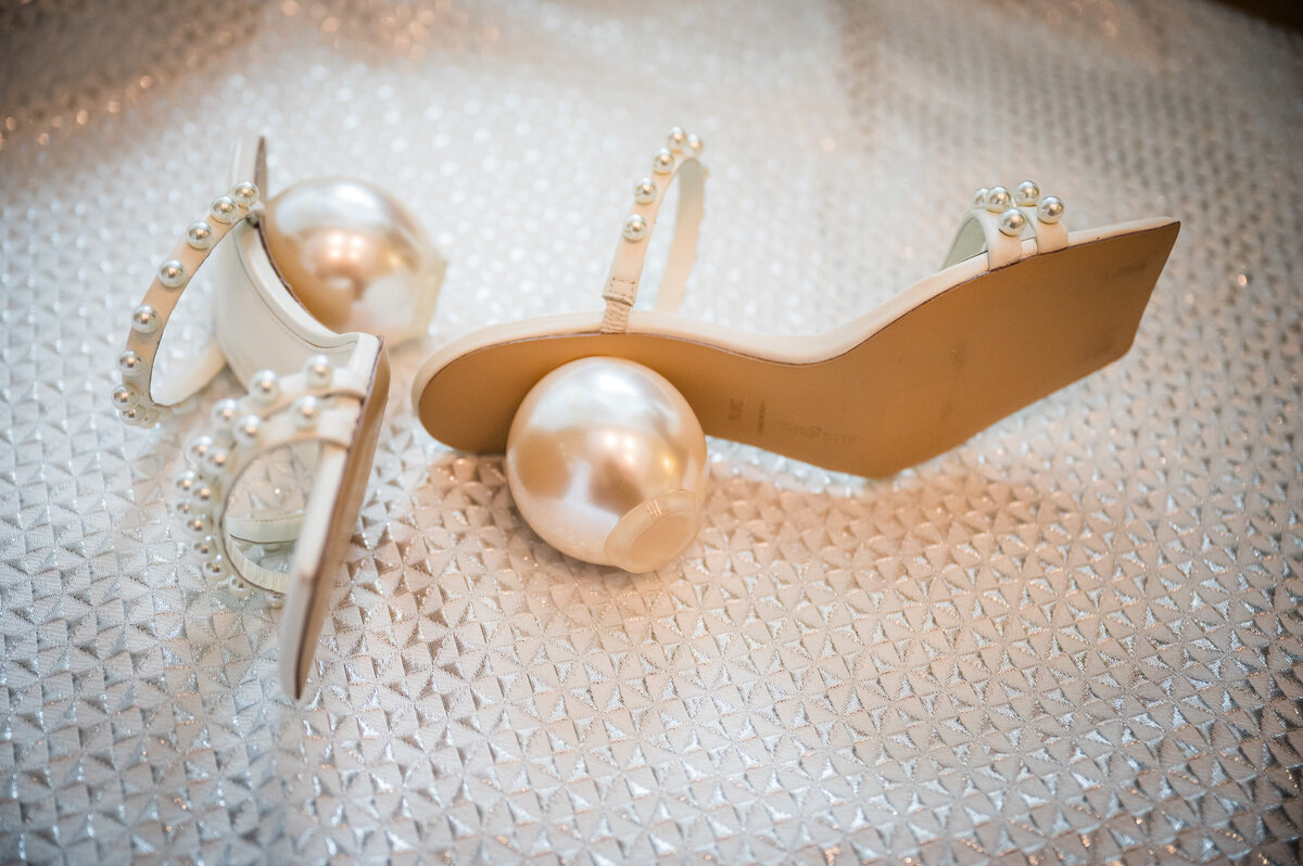 A pair of wedding heels. The heel of the shoes resembles a large pearl ball.