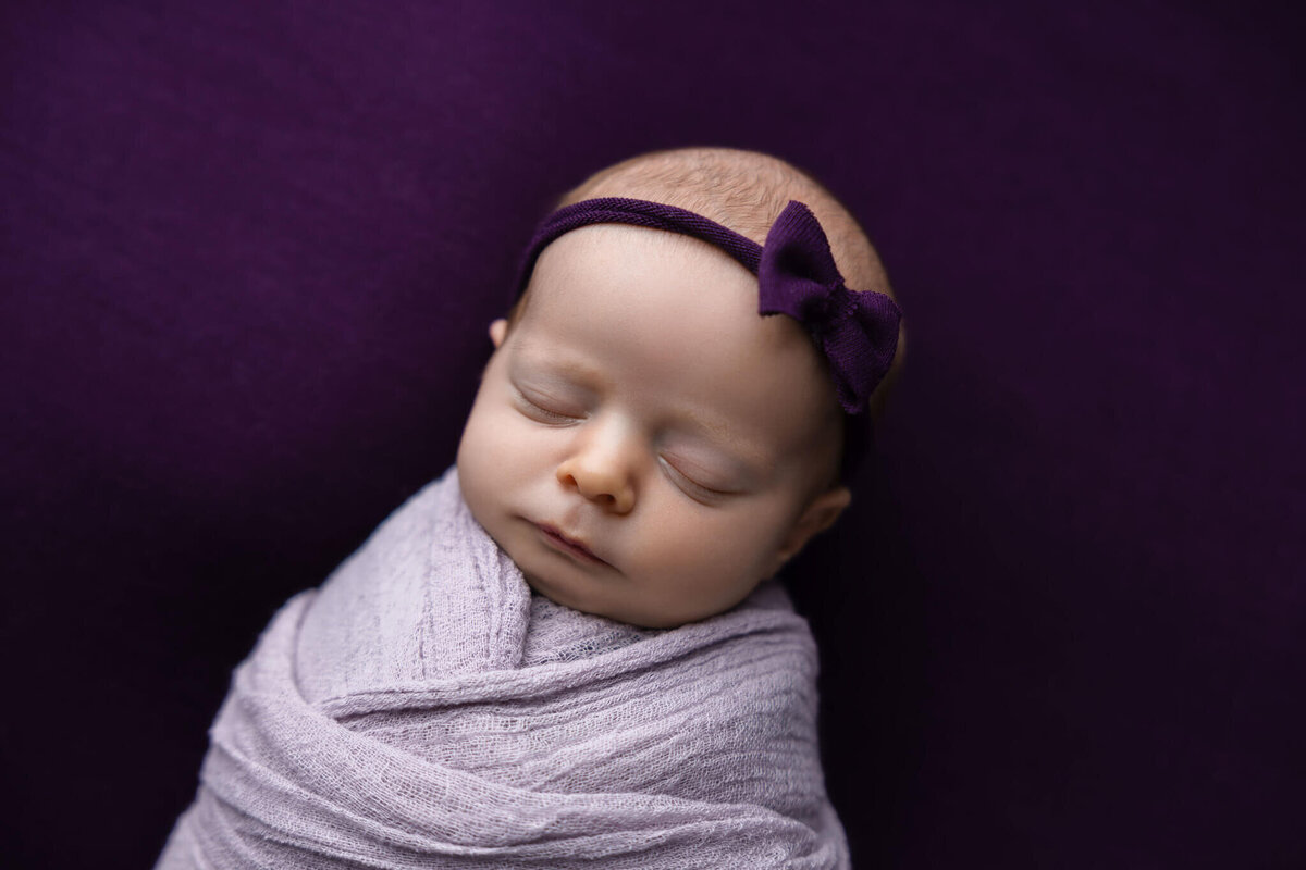 newborn baby in purple wrap with a purple headband asleep