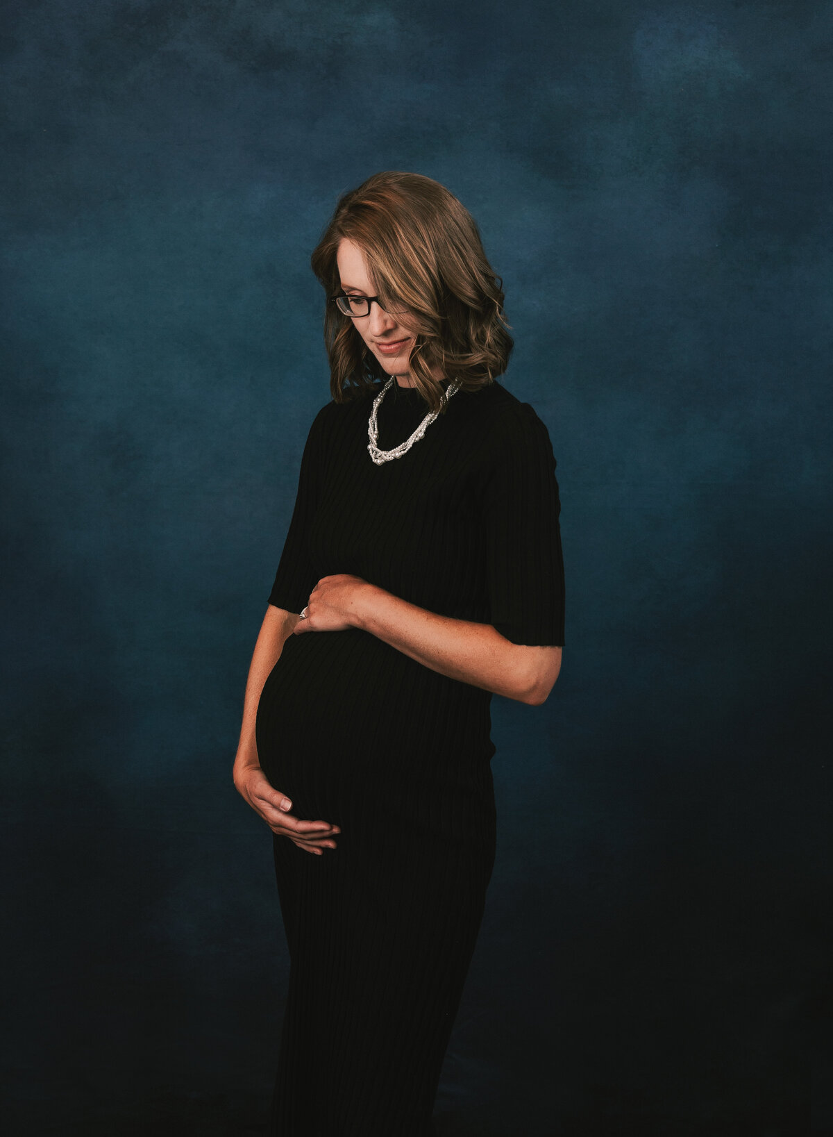 Expectant mother on a blue backdrop in a studio maternity photo.