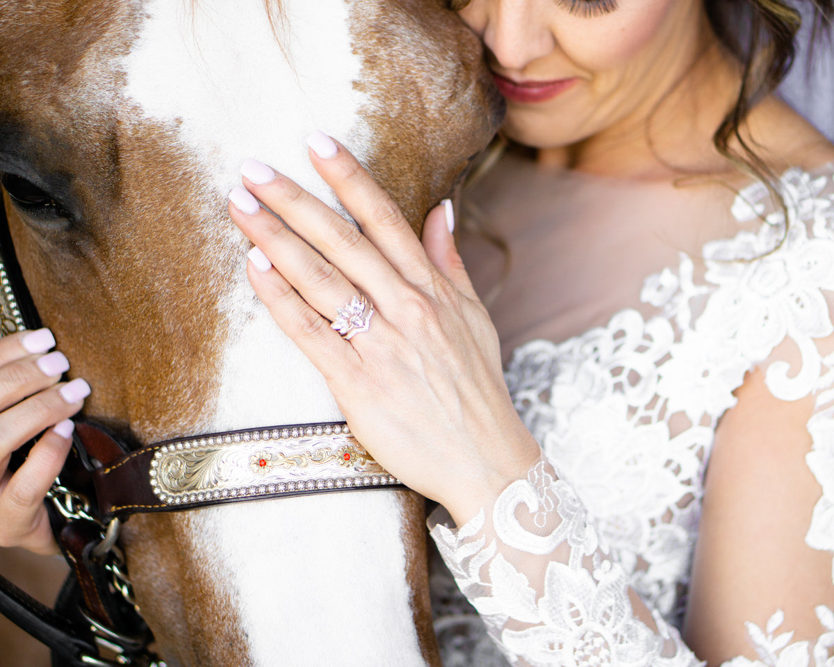 Bride nuzzling horse while showing off her ring  with her hand on his nose