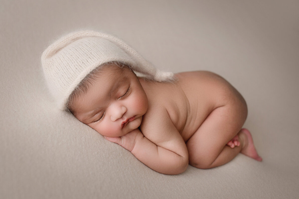 baby girl sleeping on a cream blanket wearing a sleepy hat