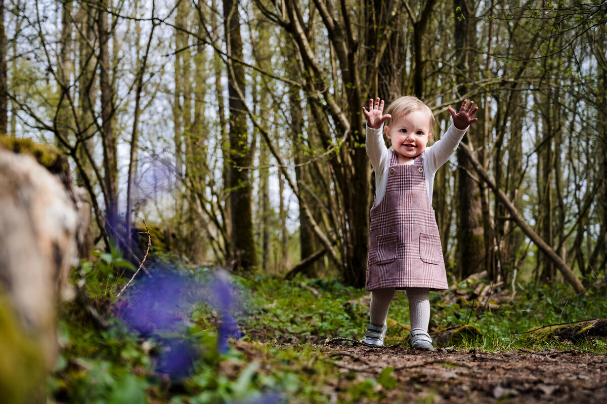 Little girl running with hands up through the bluebells