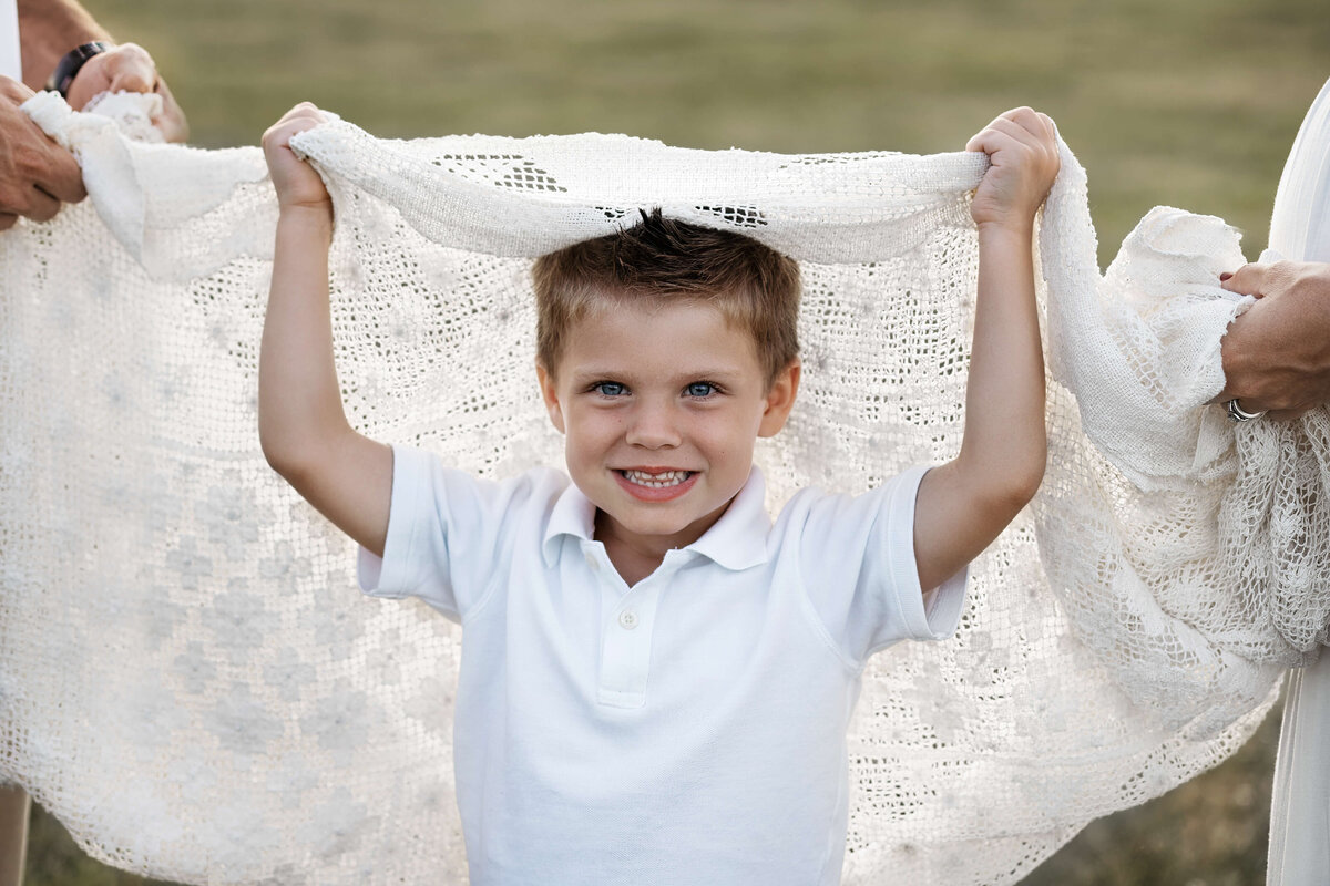 little boy holding a blanket over his head at sunset at a family photography session