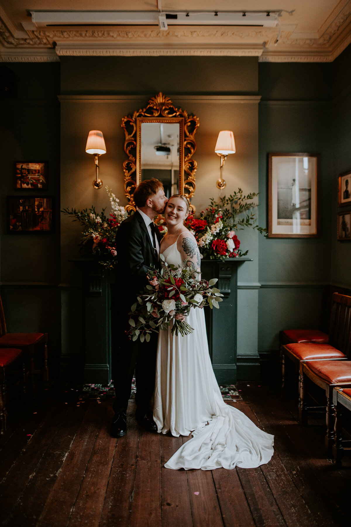 A couple stand in front of a large fireplace at their reception in London after marrying at The Old Marylebone Town Hall.