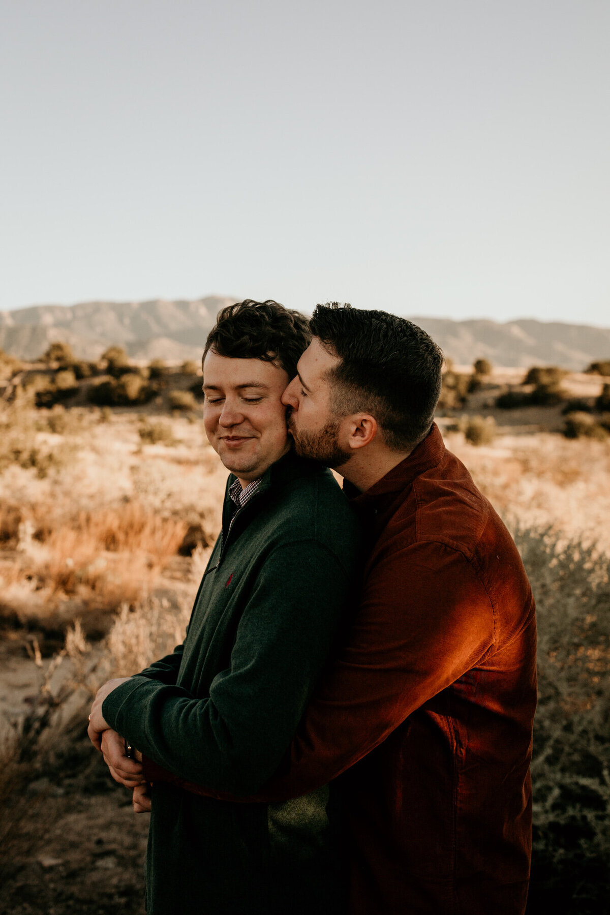 man kissing same sex fiancé on the cheek from behind
