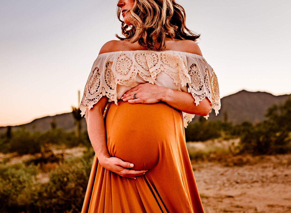 mom holding her pregnant belly for maternity photos in Arizona golden and lace boho dress