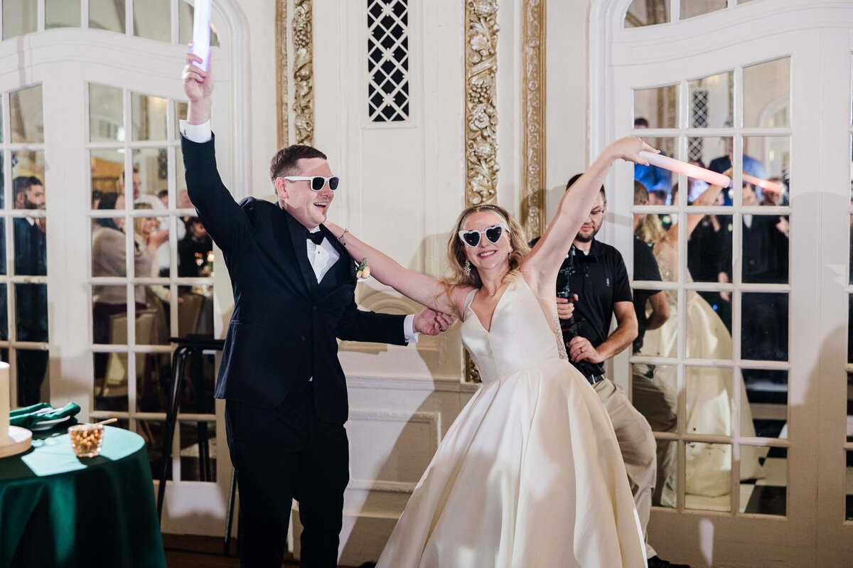 Bride and groom dancing joyfully with sunglasses on at their Iowa wedding reception, surrounded by guests.