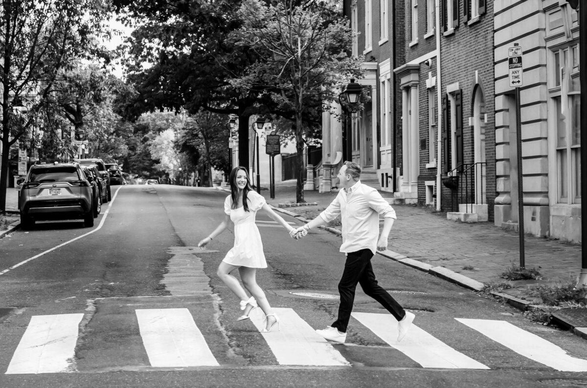 Woman in a short white dress, running across the street, while holding a man's hand in Philadelphia, PA