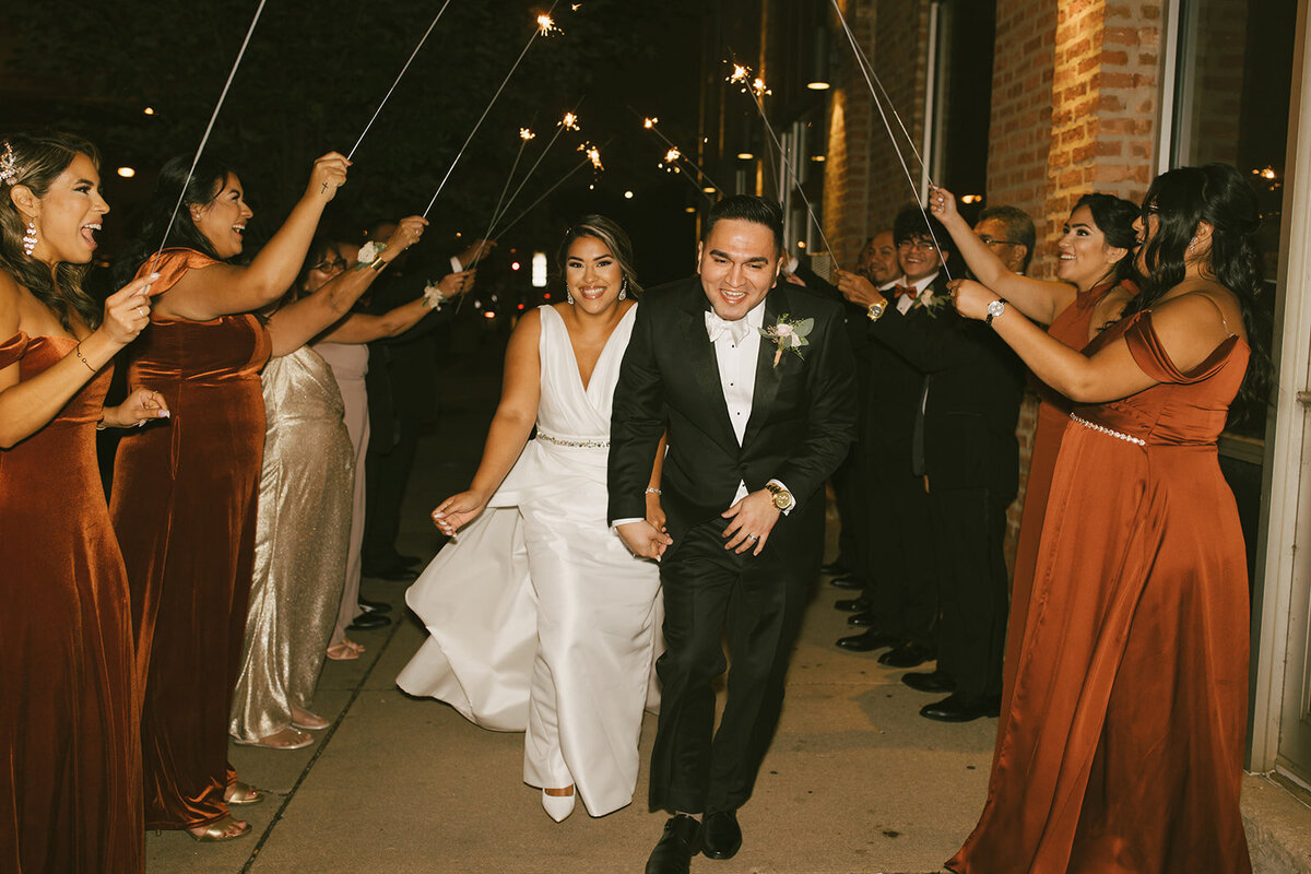 Graceful bride holds hands with groom during sparkler sendoff outside of Loft on Lake, Chicago.