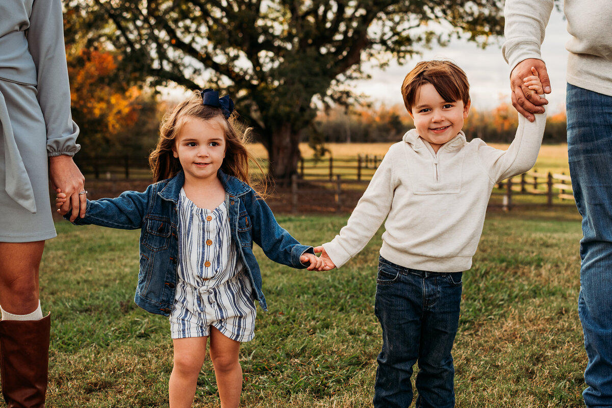 A brother and sister hold hands and smile at the camera in League City, Texas.