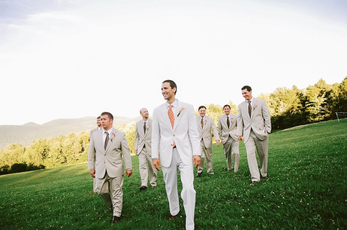 Groom and groomsmen, walking on a grassy mountain side, dressed in seersucker during a wedding at Killington vermont