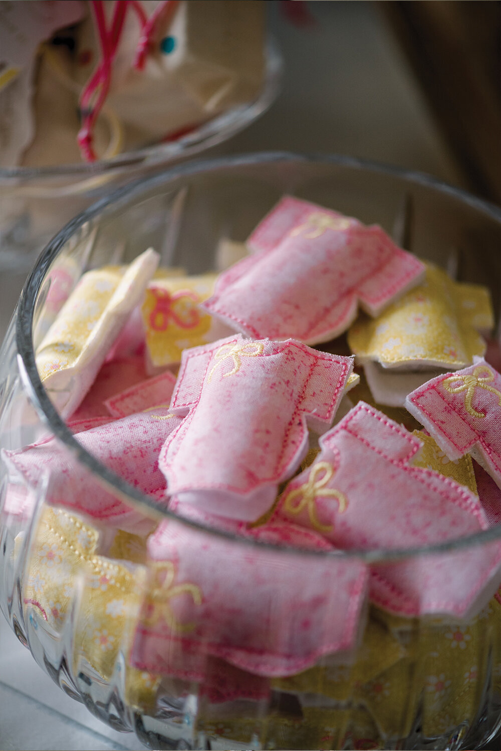 Pink and yellow fabric Hershey nugget holders elegantly arranged in a crystal bowl, showcasing the charming party favors for a girl’s baby shower.