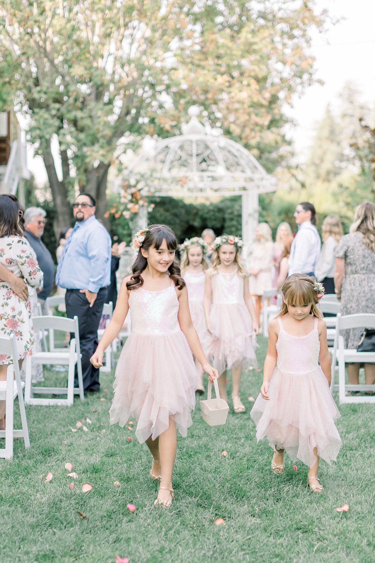 The many flower girls toss floral petals along the aisle.