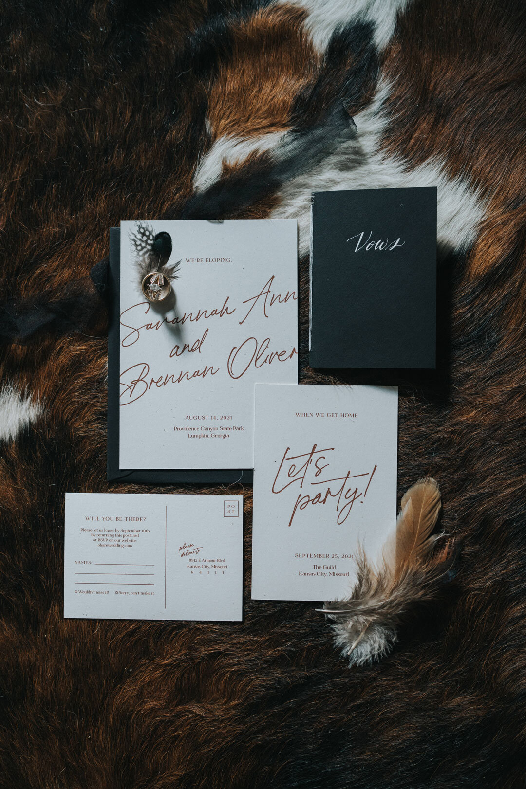 White wedding invitation with red script next to a feather and black vow book