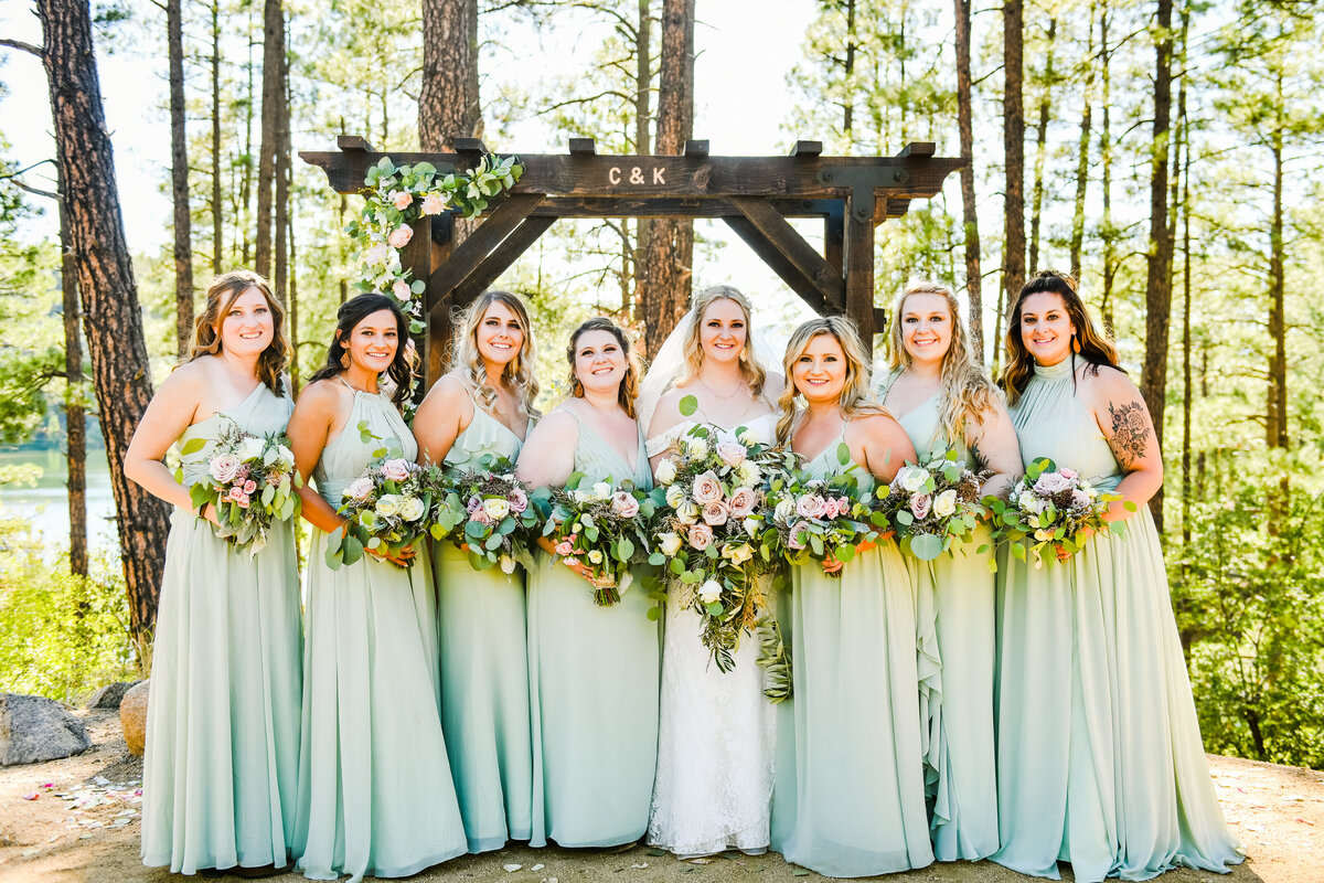Bride with Bridesmaids arch smiling holding bouquets Goldwater Lake Prescott wedding