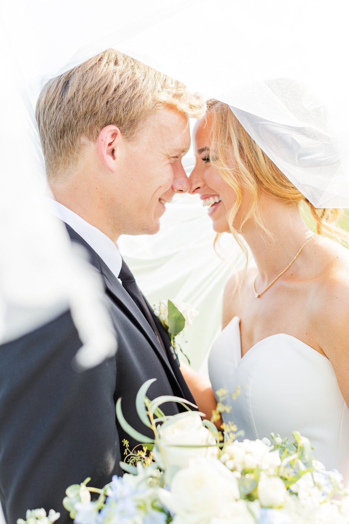 Bride and groom laughing together underneath their veil on their wedding day
