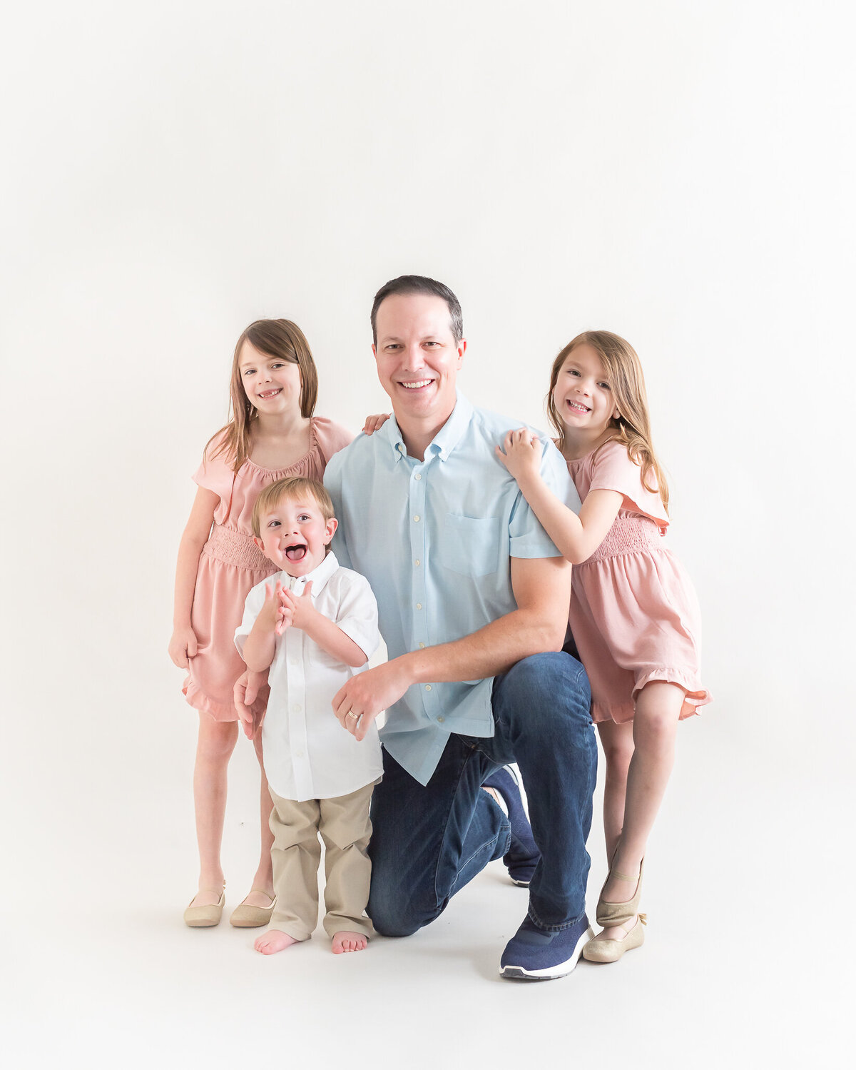 studio portrait on light bright backdrop of dad with his little kids