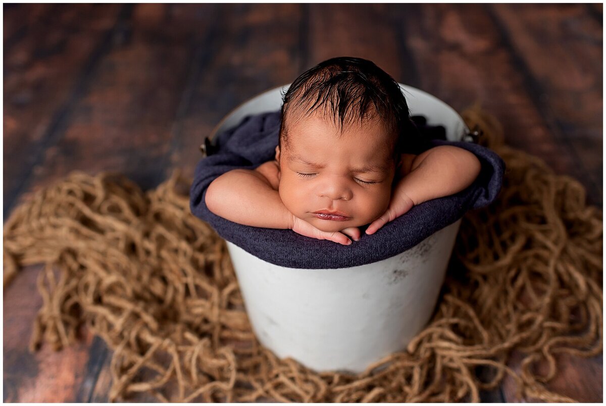 A newborn baby laying in a prop bucket, showcasing their tiny features and the preciousness of their early days of life.