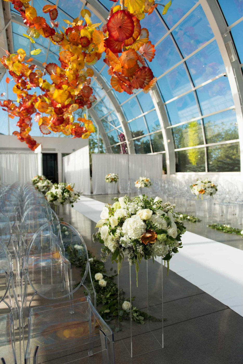White and green flowers with pops of orange are propped up on lucite stands along the aisle.