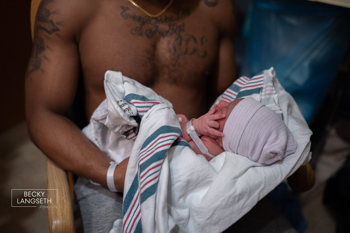 A new dad is holding his newborn at a hospital in Seattle. The baby's tiny hand is visible and almost looking like that baby is giving us the "shaka"