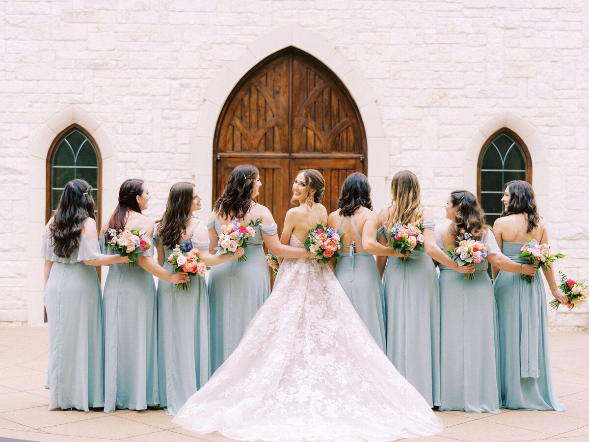 Bridal party poses showing off their aqua colored bridesmaid dresses and bride wearing Monique Lhuillier
