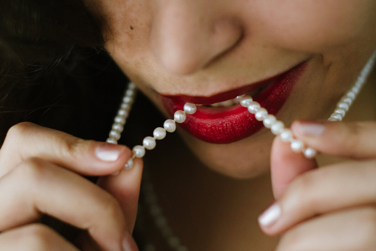 A close up view of a person biting a string of pearls on a necklace.