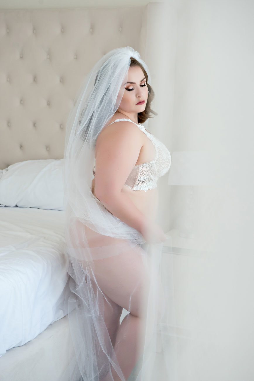 A stunning portrait of a confident and empowered plus size woman in a bridal boudoir setting, showcasing her unique beauty and celebration of her figure. This image captures the essence of inclusivity and body positivity in the lead up to the big day. Perfect for anyone looking to celebrate beauty in every size in their bridal boudoir experience.