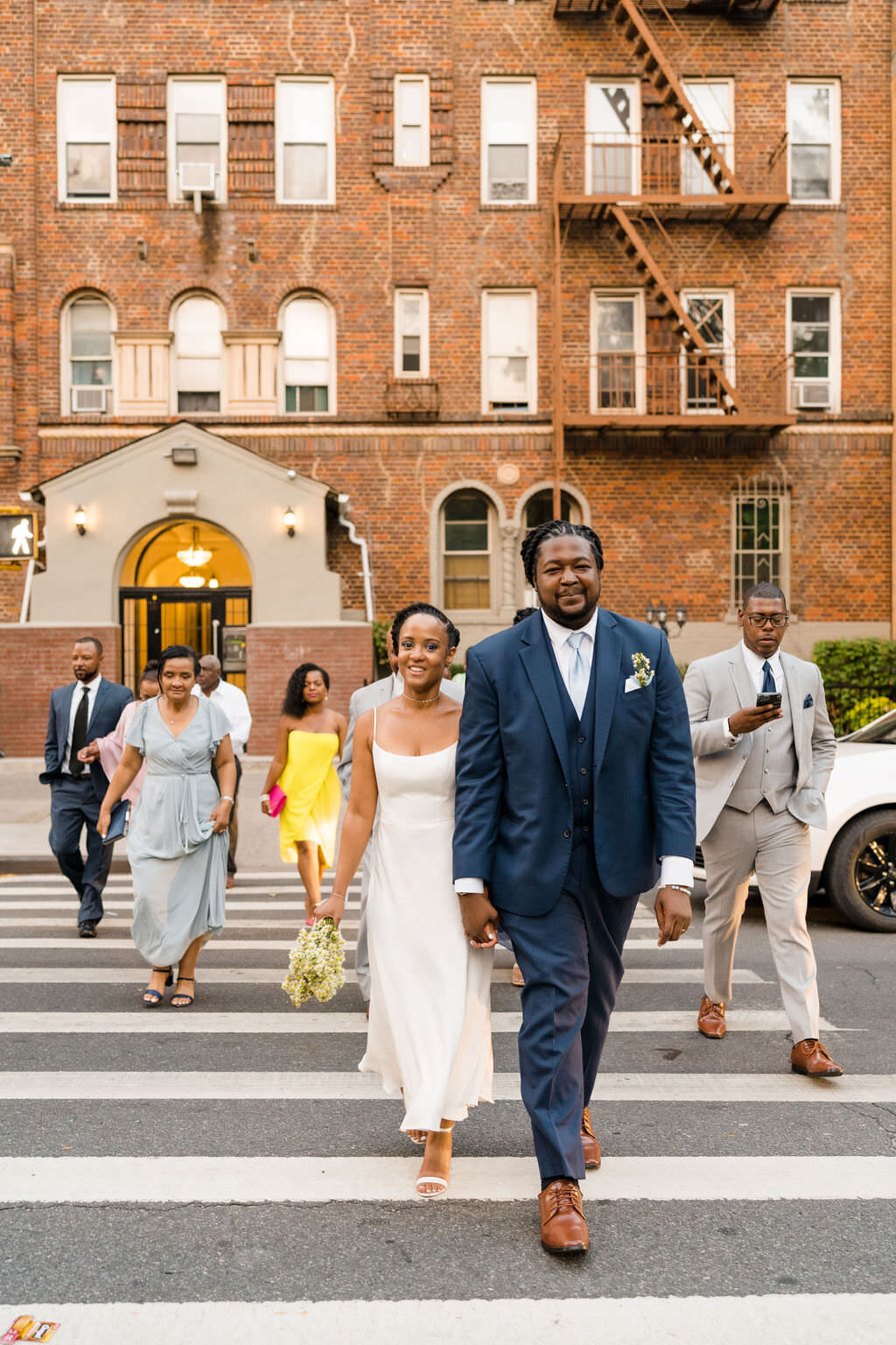 bride and groom walking across a crosswalk with their family following behind
