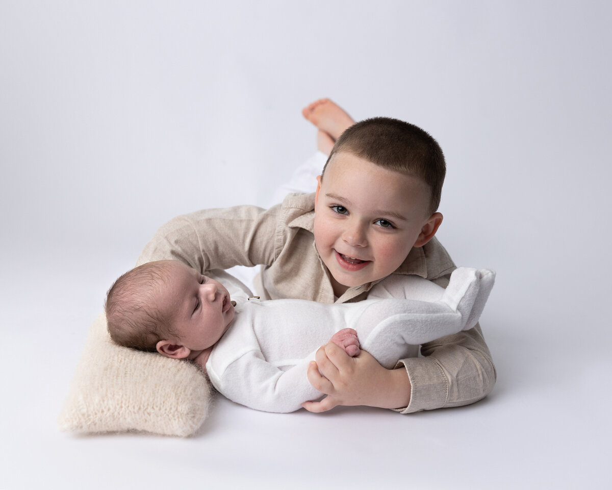 Toddler laying down holding newborn in his arms for a sibling portrait in Greensburg